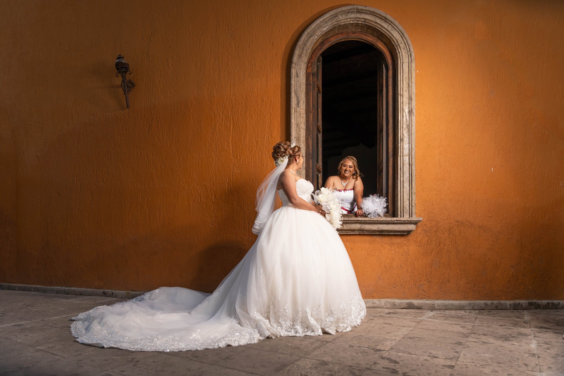 Una novia y su reflejo en un espejo, frente a un muro color ocre